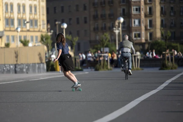 一个溜冰的少女和一个骑自行车穿过城市的老人 — 图库照片