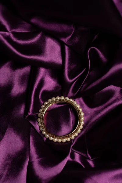 紫色の絹の布の背景に大理石の石と黄金のブレスレットの垂直ショット — ストック写真