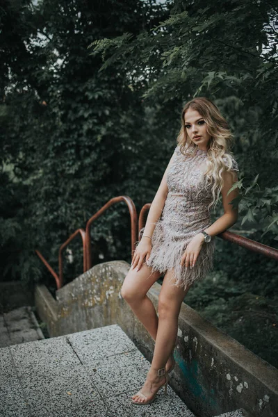 一位年轻的金发女子穿着雅致的米色花边裙 站在花园的楼梯上 — 图库照片