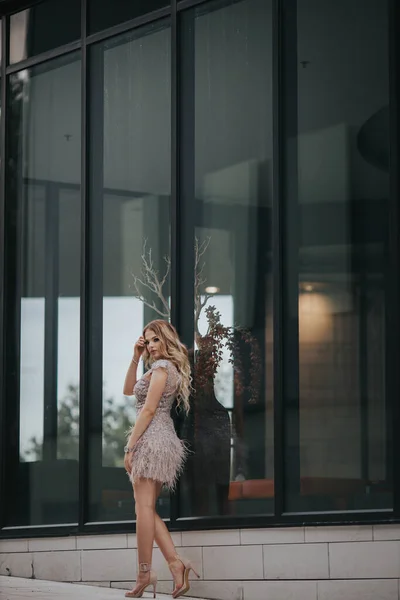 エレガントなベージュのレースドレスを着た若いブロンドの女性がガラスのドアの前に立っている — ストック写真