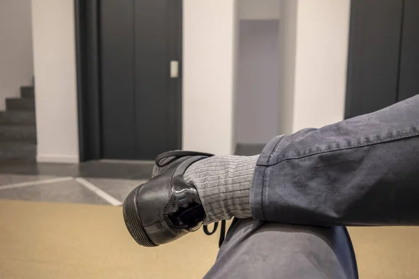 One Man with Legs Crossed with a Shoe in Front of and Elevator Door in Switzerland.