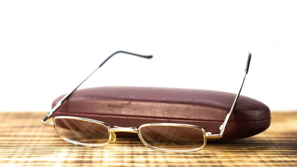 A shot of the eyeglasses with case on a wooden base in a white background.