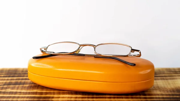 A shot of the eyeglasses with a case on a wooden base with white background.