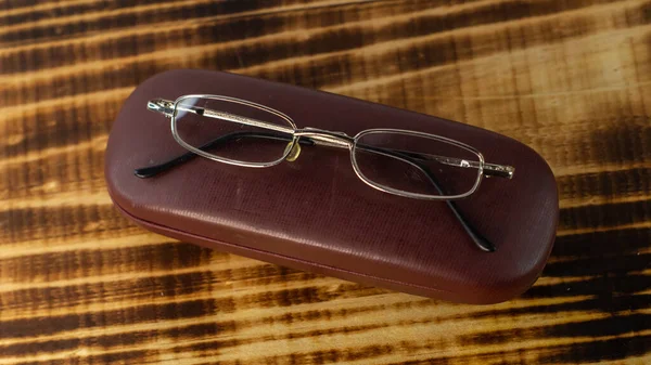 A shot of the eyeglasses with case on a wooden base in a white background.
