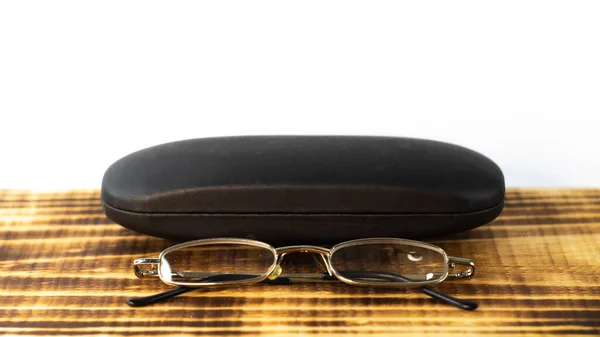 A shot of the eyeglasses with the case on a wooden base in a white background.