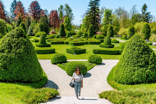 Young woman walking on path in beautiful green park with hedge shapes and trees at Arboretum volcji potok near Radomlje in Slovenia.