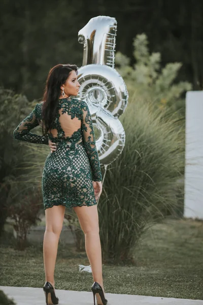 一个穿着绿色鸡尾酒花裙 穿着银色18号气球的性感高加索女人的竖直照片 — 图库照片