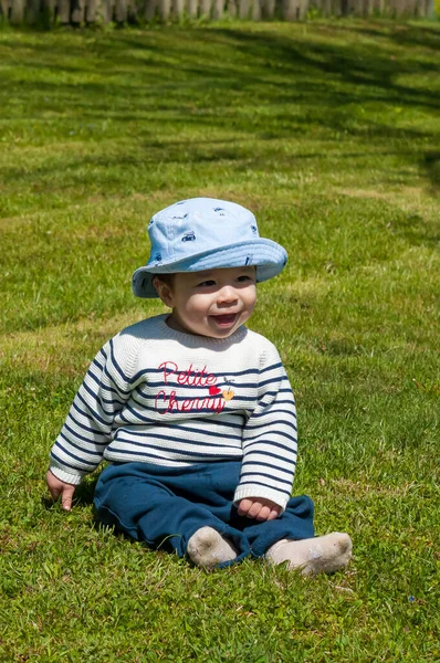 草の上に座っている帽子の中にかわいい幸せな男の子の垂直ショット — ストック写真