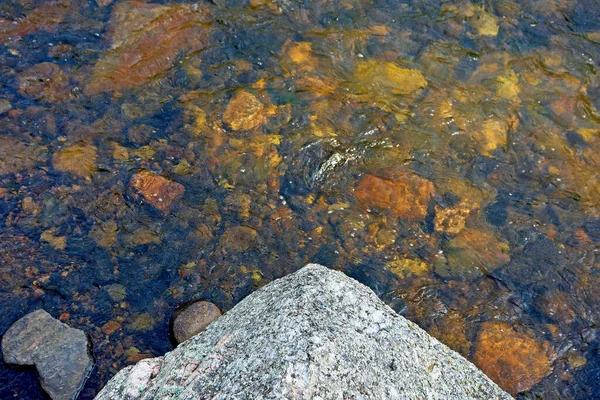 在阳光下被湖水环绕的高角形岩石 — 图库照片