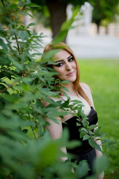 一个年轻的高加索女性站在绿叶树旁的一张垂直的照片 — 图库照片