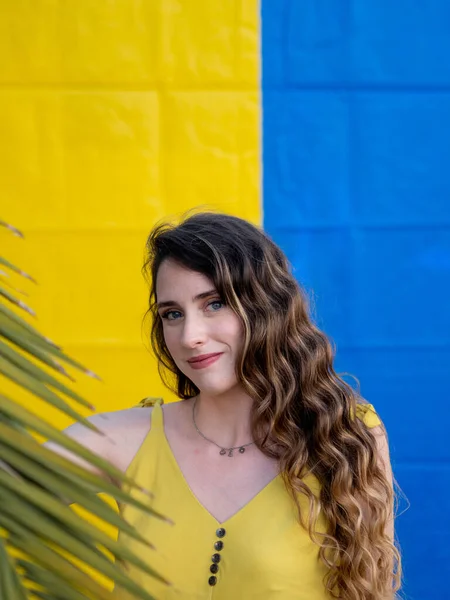 一个年轻迷人的白种人女子在蓝色和黄色的墙壁附近摆姿势的垂直特写镜头 — 图库照片