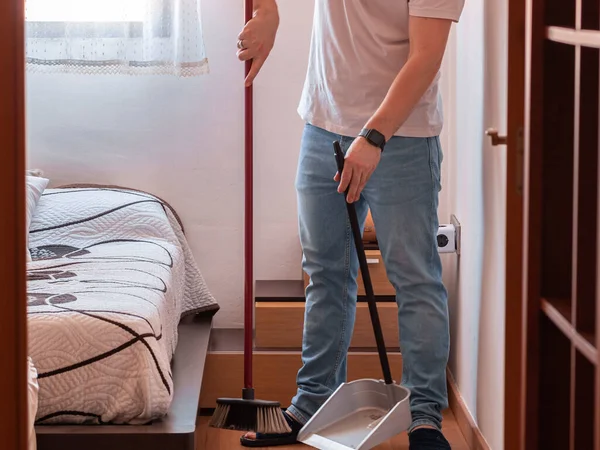 A utility man with a broom and dustpan cleaning the floor