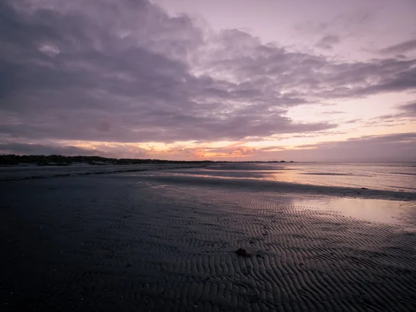 夕暮れ時の湿った砂浜に反射するオレンジ色の夕日の曇り空の美しい景色 — ストック写真
