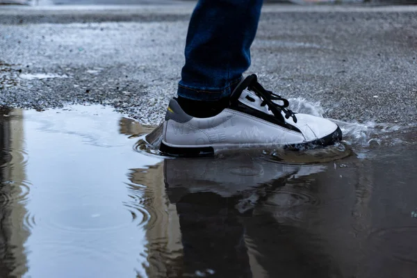 一个穿着白色运动鞋站在水坑里的人的特写镜头 — 图库照片