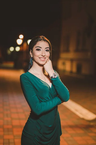 一张白色的年轻女子在夜晚穿着雅致的绿色衣服在街上摆姿势的垂直照片 — 图库照片