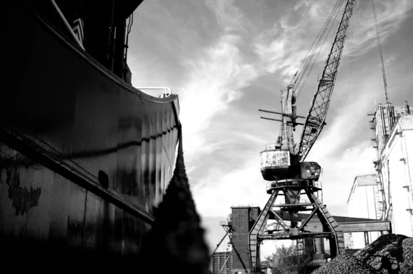 A grayscale shot of cranes at an industrial site against a cloudy sky