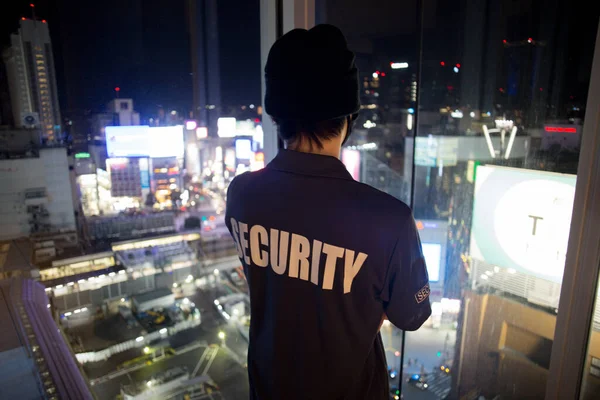A closeup shot of a security guard looking down the cityfull of lights at night.