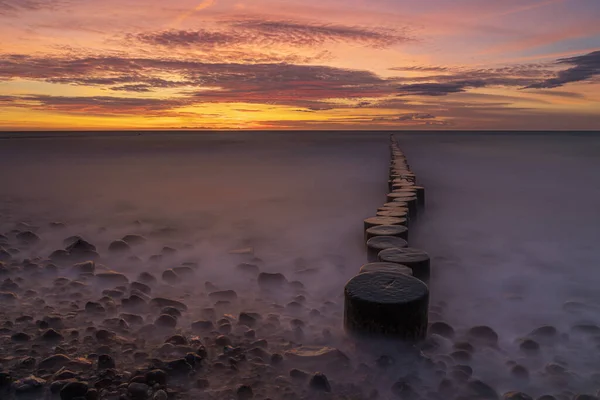 stock image Beautiful sunset over a tranquil sea with wooden logs