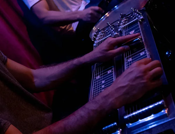A shallow focus of a man playing pedal steel guitar