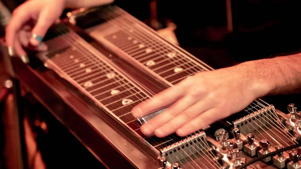 A shallow focus of a man playing pedal steel guitar