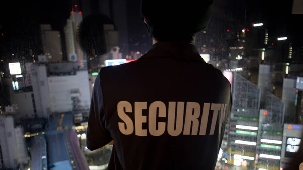 A closeup shot of a security guard looking down the cityfull of lights at night