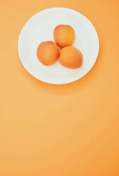 Colpo Verticale Tre Albicocche Fresche Piatto Isolato Fondo Arancione — Foto Stock