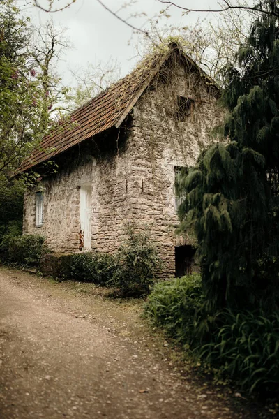 暗い空の下で緑の木々や植物に囲まれた古い石造りの家の垂直ショット — ストック写真