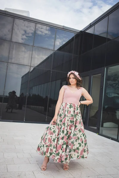 一位漂亮的高加索女人 身穿雅致的长花裙 背景在一座现代建筑上 — 图库照片