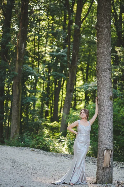Привлекательная Белая Женщина Элегантном Длинном Серебряном Платье Опирающемся Высокое Дерево — стоковое фото