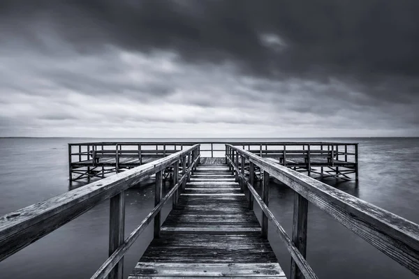 Dramatisk Gråskala Väderbiten Brygga Havet Bakgrunden Den Molniga Himlen — Stockfoto