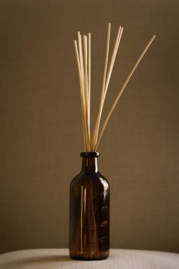 A dark glass diffuser bottle with natural reed sticks put on a pillow clipart