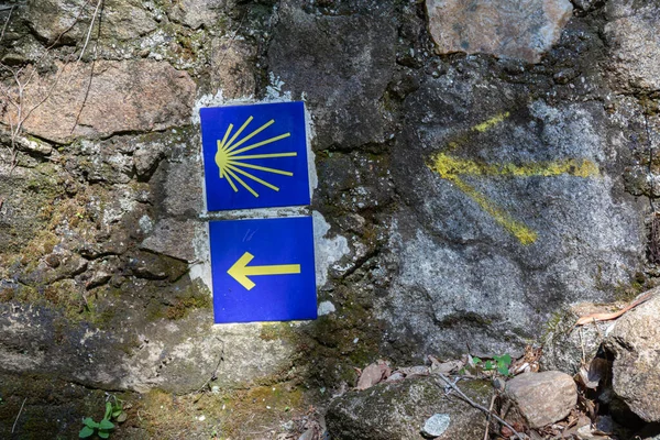 Camino de Santiago sign tiles on stone wall. Yellow arrow and shell symbol