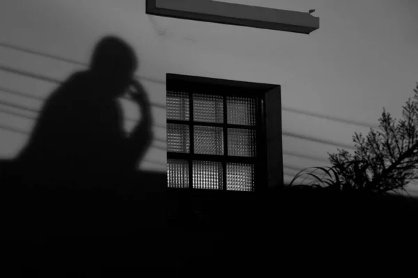 一个心事重重的人在窗边的白墙上抽烟的影子 — 图库照片