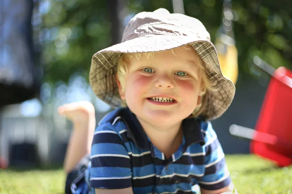 幸せな可愛いですブロンドオーストラリアの子供は遊び場で草の上に横たわっています — ストック写真