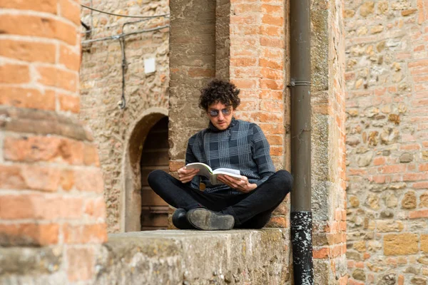 一个年轻的意大利男人双腿交叉坐在一起看书 — 图库照片
