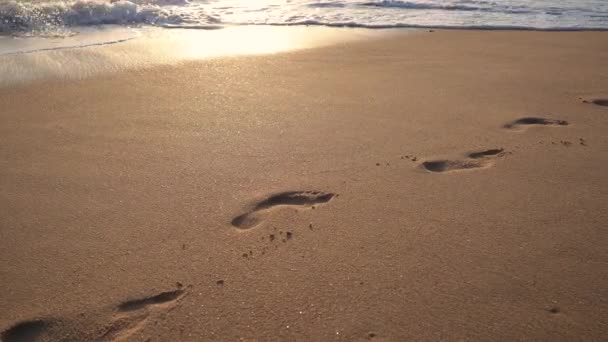 砂浜で波が砕ける4Kショットと日没時の人の足跡を消す — ストック動画