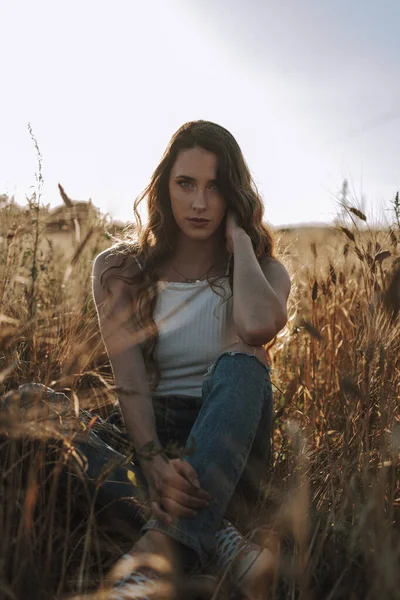 太陽が彼女の後ろに輝くと小麦畑でカメラを見て見事なスペインの女の子の垂直ショット — ストック写真