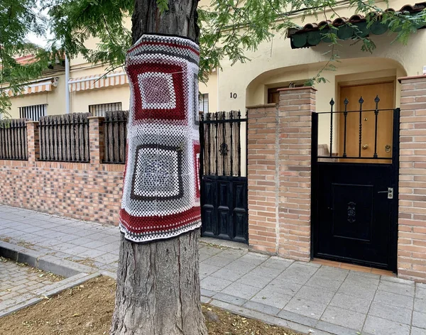 A closeup shot of yarn bombing on a tree next to a cottage