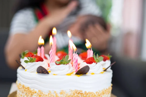 背景には ろうそくに火を灯した苺の誕生日ケーキと新生児を抱える思いやりのある母親 — ストック写真