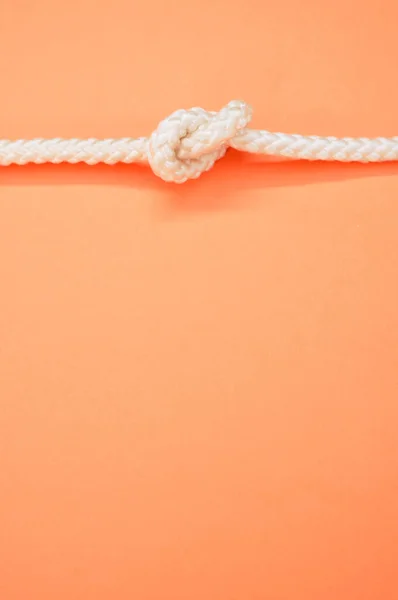 Вертикальный Снимок Белой Веревки Узлом Горизонтально Изолированным Пастельно Оранжевом Фоне — стоковое фото