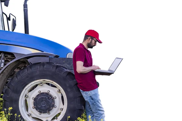 A young farmer using a laptop in front of a blue tractor isolated on white - smart agriculture concept