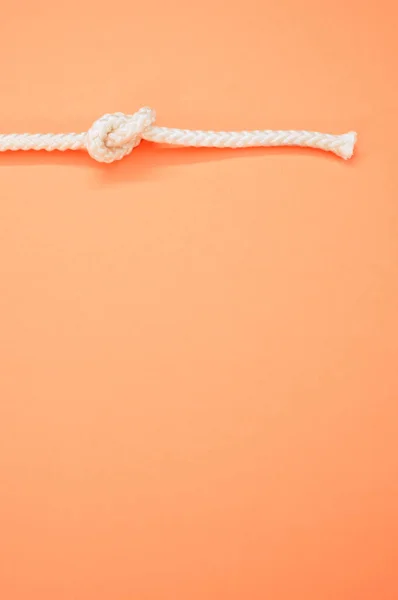 Pionowe Ujęcie Białej Liny Węzłem Odizolowanym Pastelowym Pomarańczowym Tle — Zdjęcie stockowe