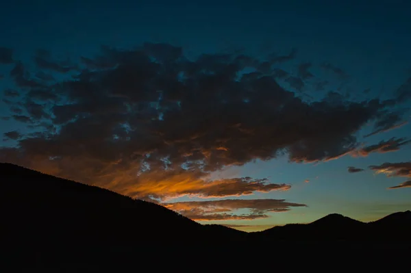 オレンジと青の色合いの夕日の曇りの空を背景に山脈のシルエット — ストック写真