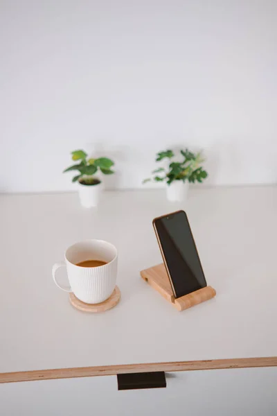 木製の板の上に白いカップと電話の垂直ショット — ストック写真