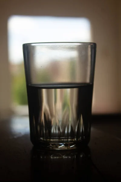 Eine Vertikale Aufnahme Eines Halbvollen Wasserglases Auf Dem Tisch Drinnen — Stockfoto