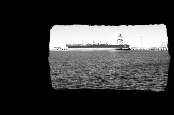 古い潜水艦の窓から見た海上の貨物船のグレースケールショット — ストック写真