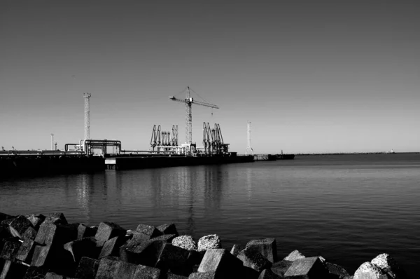 Graustufenaufnahme Eines Steinhaufens Ufer Mit Einem Kran Hinter Einem See — Stockfoto