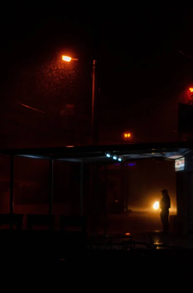屋根の下にカラフルな光と人が立って雨の夜の垂直ムーディーショット — ストック写真