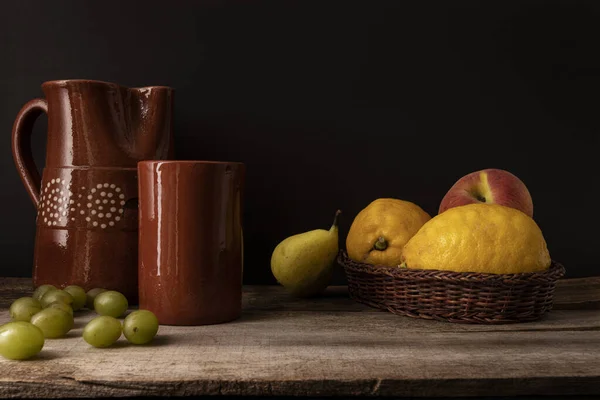 A wooden table with a thatch fruit basket and clay pots arranged on it for painting