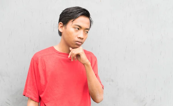 Zamyšlený Indonéský Chlápek Červeném Tričku Šedé Zdi — Stock fotografie